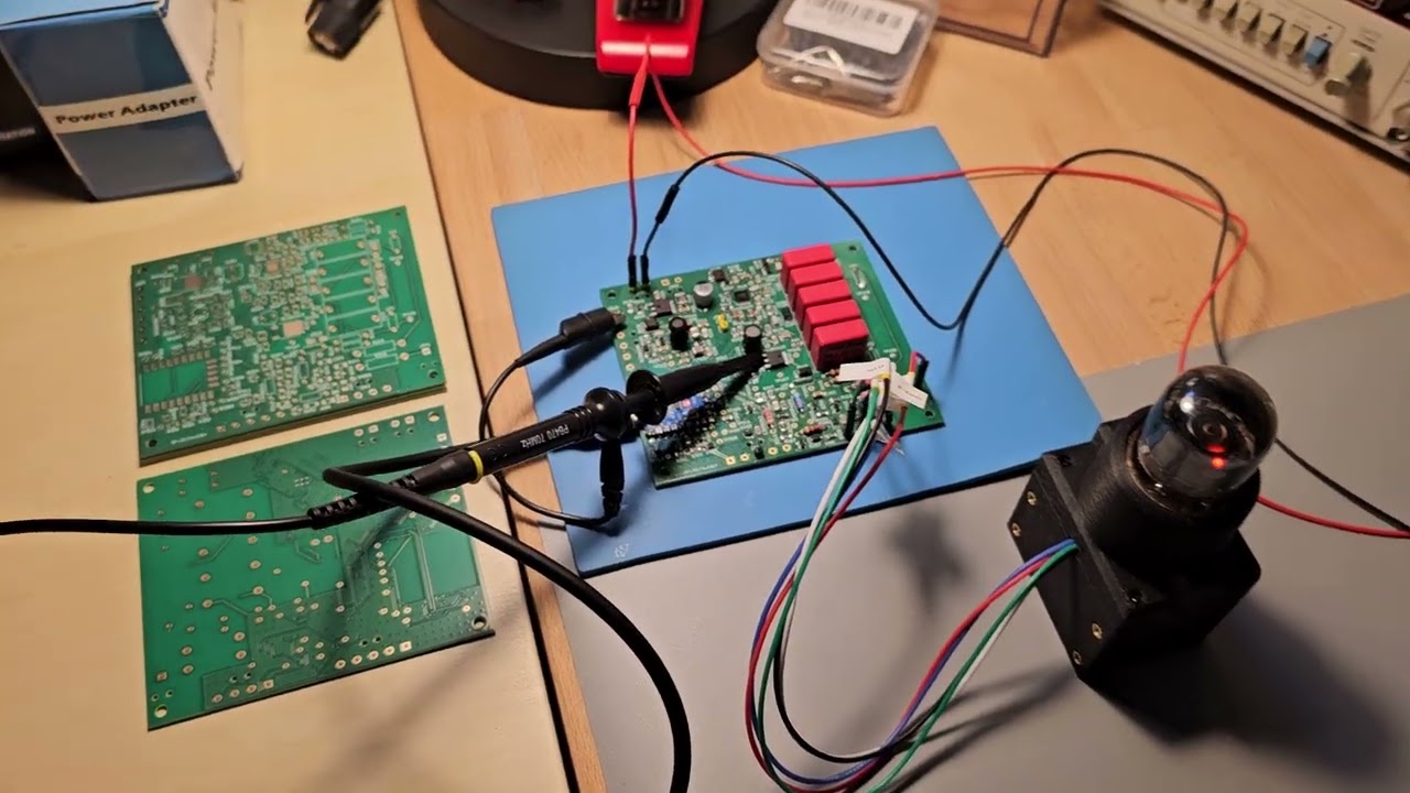 Still from the video: the assembled controller/PSU board on a blue mat with scope probes attached, wired to the A101 in its socket housing, the glow lit; two bare boards lie alongside